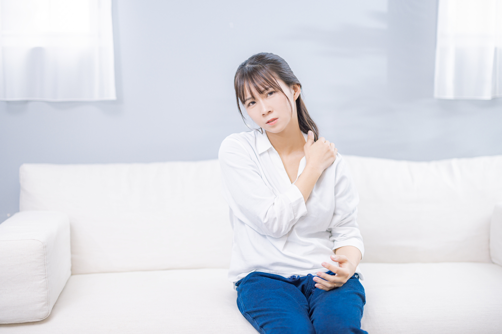 自宅のソファでおなかを押さえてつらそうにする女性